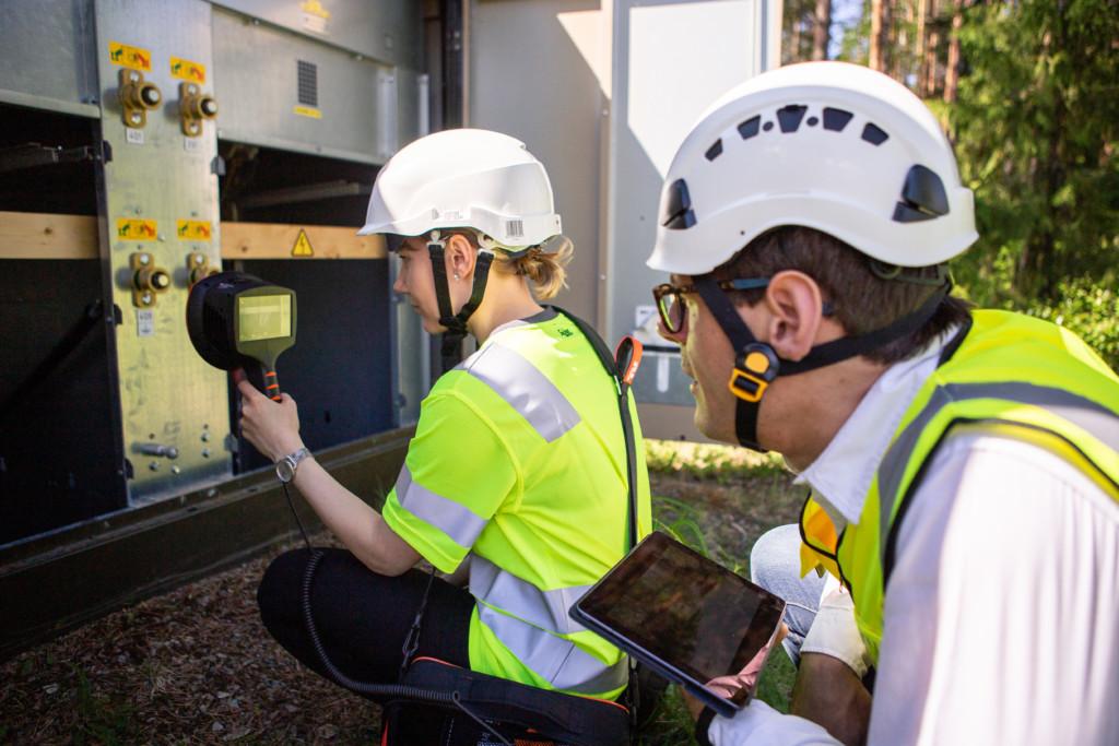 Female maintenance worker detecting partial discharges with ultrasonic acoustic NL Camera. Male worker supervises.